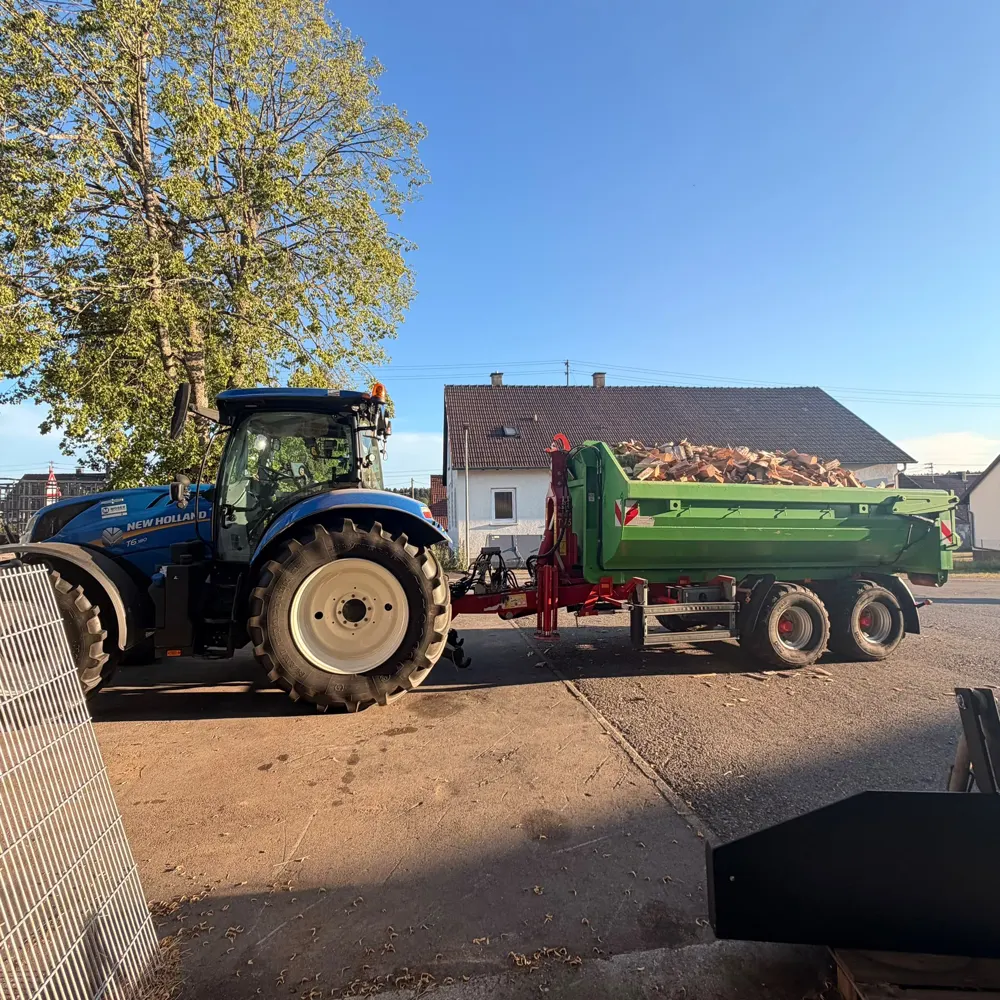 Traktor mit Kipper, beladen mit gespaltenem Brennholz